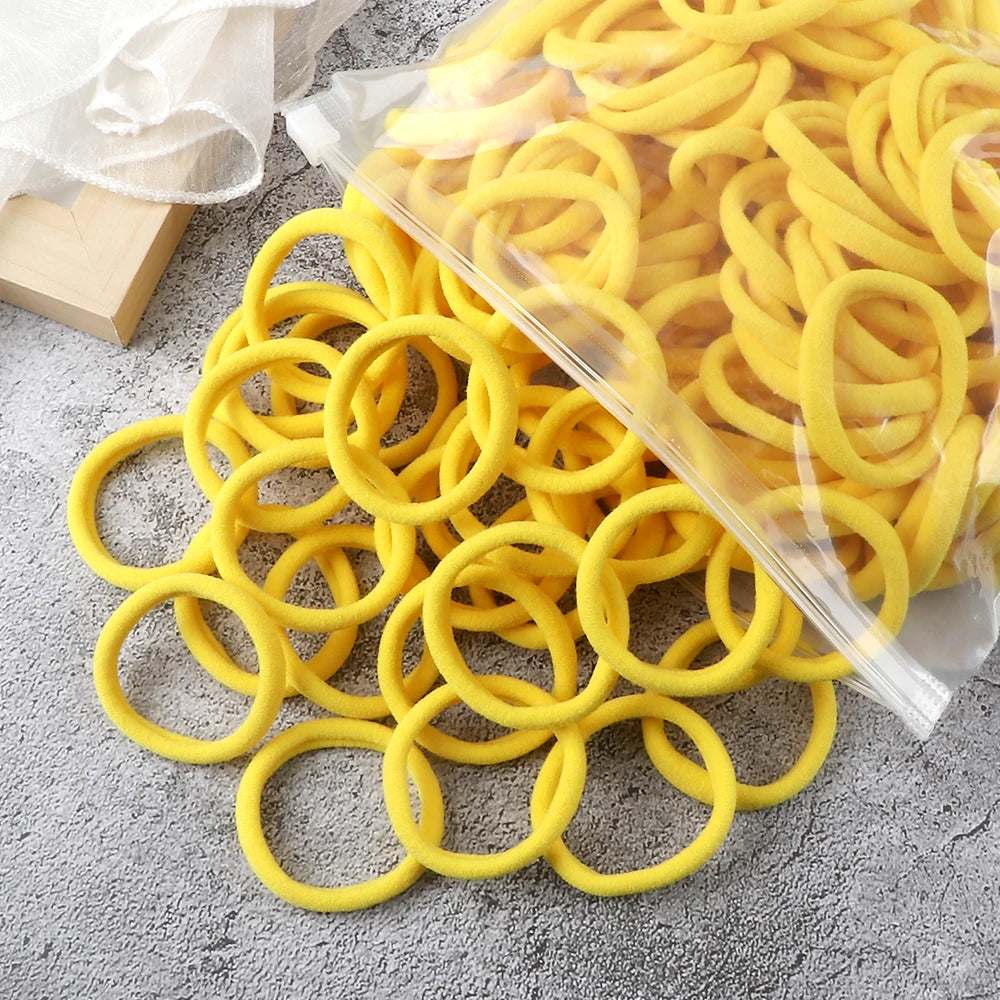 A pile of yellow elastic hair bands is shown, some loose and others packaged in a clear plastic bag.