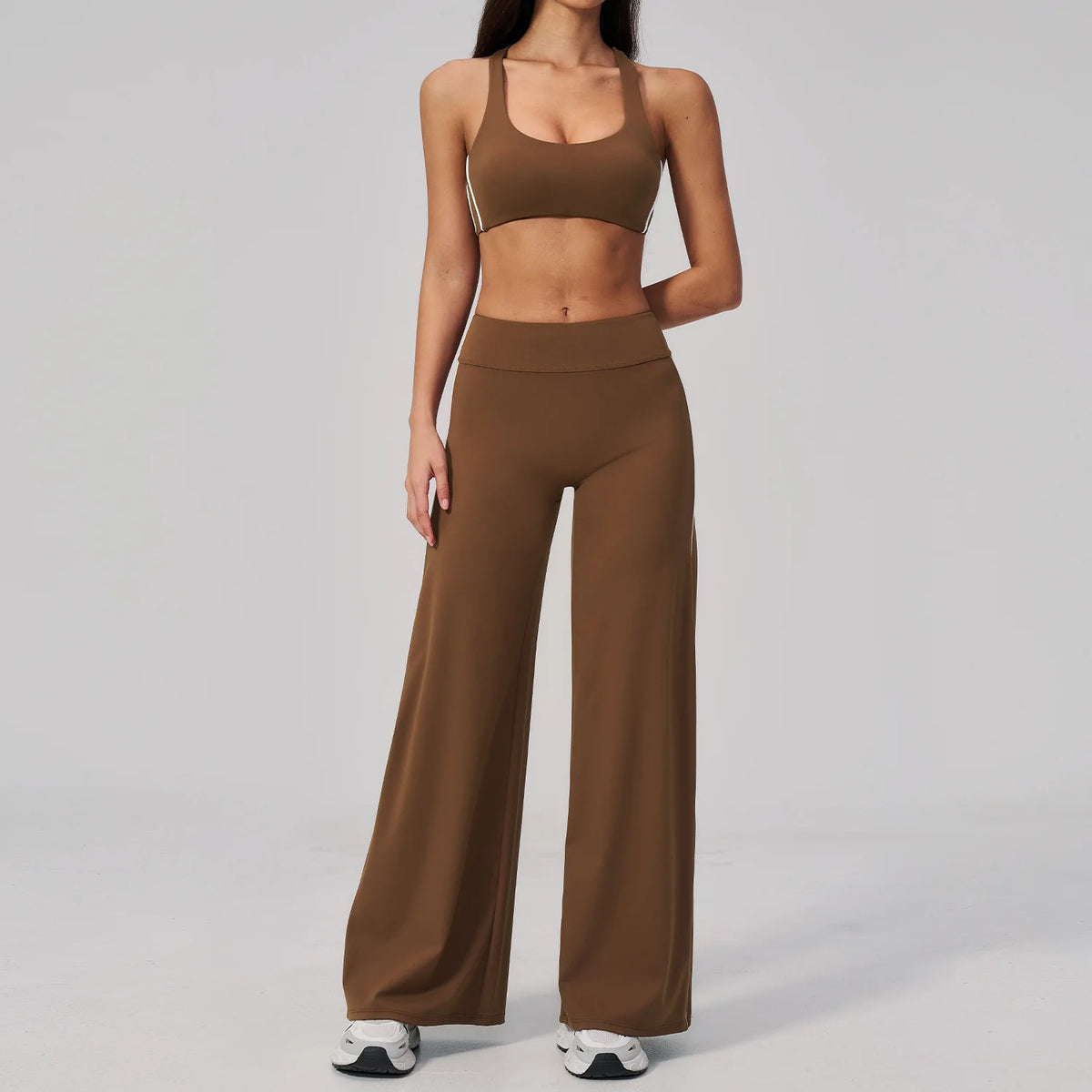 A woman wearing a brown two-piece yoga and sports tracksuit set consisting of a cropped top and matching long pants.