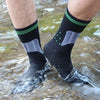 A person wearing black hiking socks with green trim is walking through shallow water.