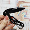 A hand holds a black folding stainless steel survival knife against a light background.