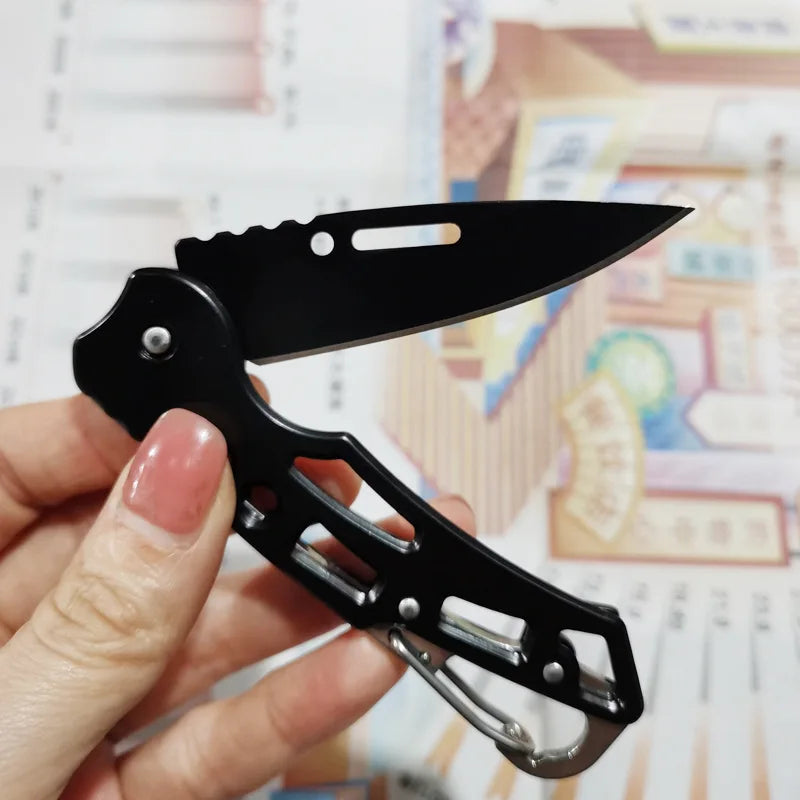 A hand holds a black folding stainless steel survival knife against a light background.