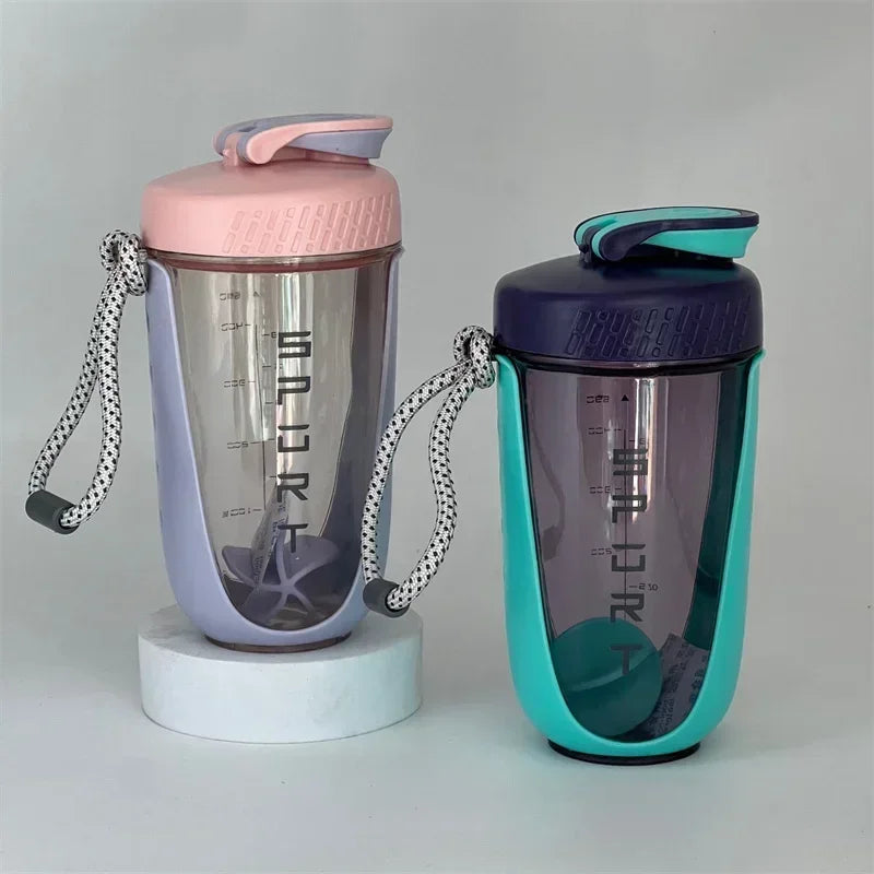 A purple and teal blender shaker bottle with a pink lid is shown standing on a white base.