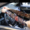 A person wearing patterned tattoo arm sleeves is driving a car, with the interior visible through the windshield.