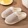 A pair of beige plush fleece slippers resting on a wooden surface next to a yellow plate.