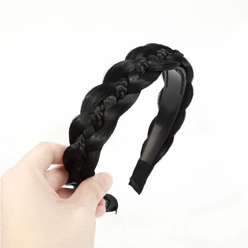 A hand holds a black twisted braided wig headband against a white background.