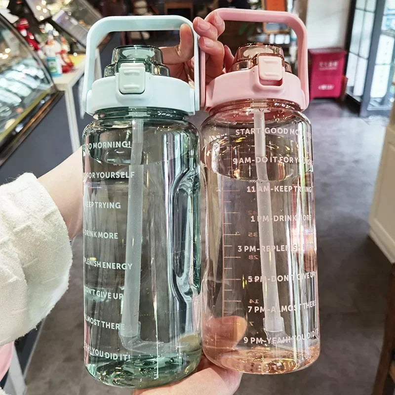 A person holds two large capacity insulated water bottles, one clear and one pink, both with straws.