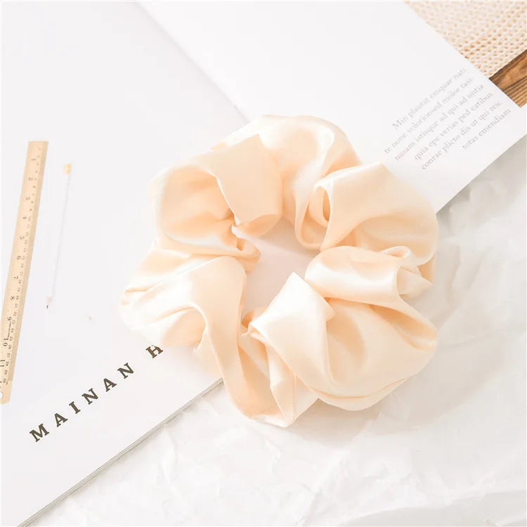 A light peach satin scrunchie is displayed on a white background next to a ruler and text.