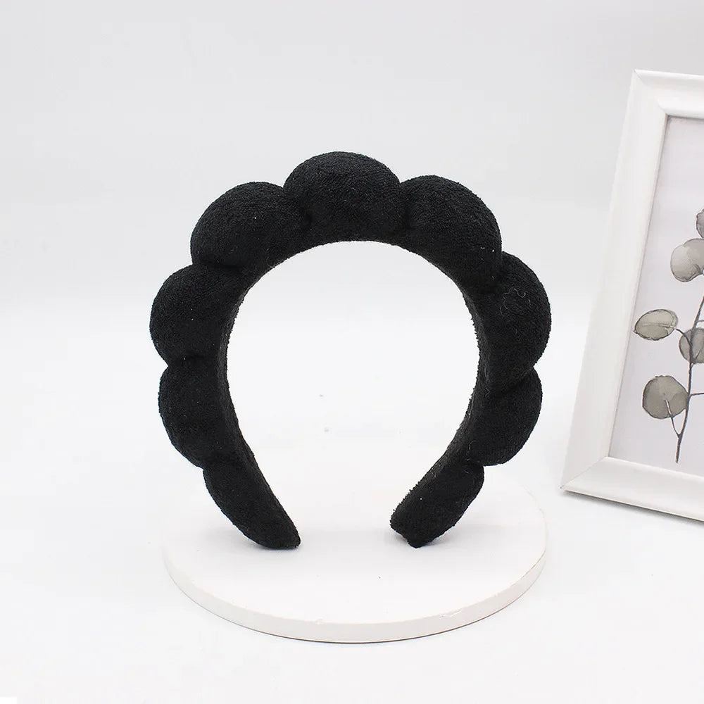 Black sponge terry cloth headband for hair styling displayed on a white circular stand.
