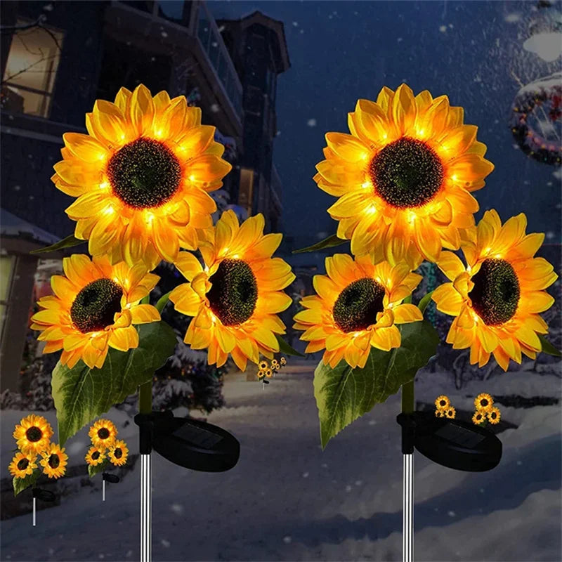 Three solar sunflower LED stake lights with yellow petals and dark centers are displayed against a snowy night background.