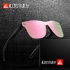 Pink and green frameless sports sunglasses resting on a black surface next to a black box.