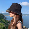 A woman wearing a black double-sided wide brim bucket hat looking out over the ocean from a scenic viewpoint.