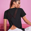A woman wearing a black breathable summer yoga and fitness t-shirt with sheer paneling, posing against a pink background.