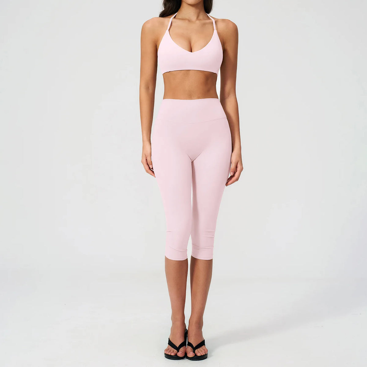 A woman models a light pink women's premium fitness tracksuit consisting of a sports bra top and matching leggings.
