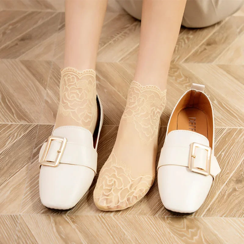 A pair of beige lace mesh ankle socks worn on feet against a light wooden floor.