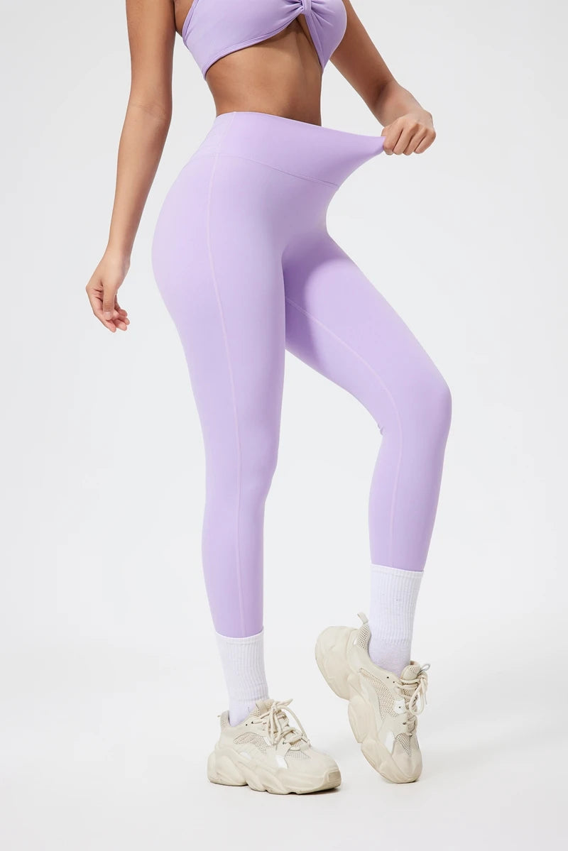 Model in seamless purple yoga leggings and matching crop top, looking down.