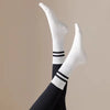 White non-slip yoga socks with black stripes worn on a person's foot and ankle.
