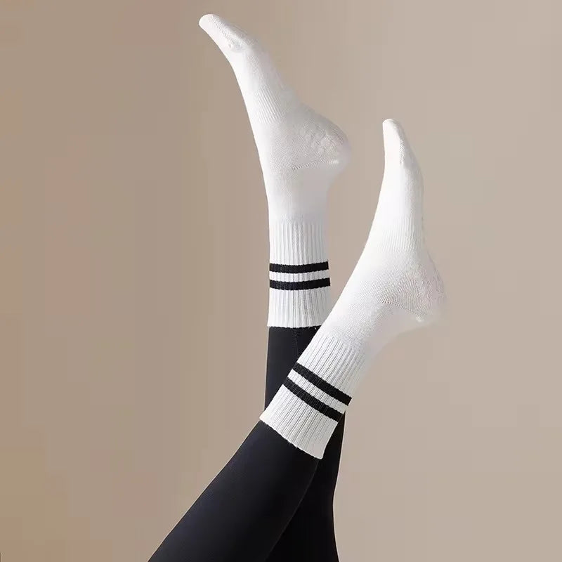 White non-slip yoga socks with black stripes worn on a person's foot and ankle.