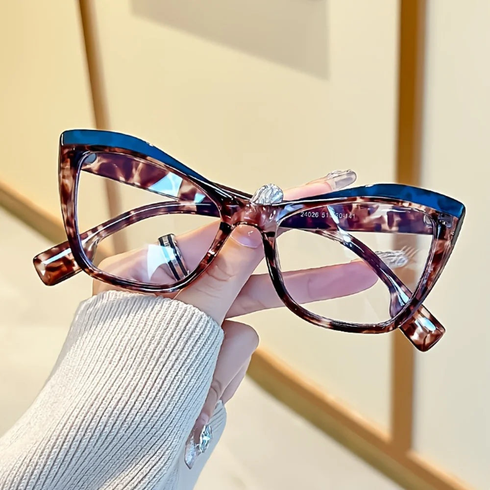A hand holds a pair of vintage color block blue light blocking eyeglasses with brown and purple marbled frames.