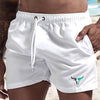 White quick-drying men's swim shorts worn by a person standing on a beach.