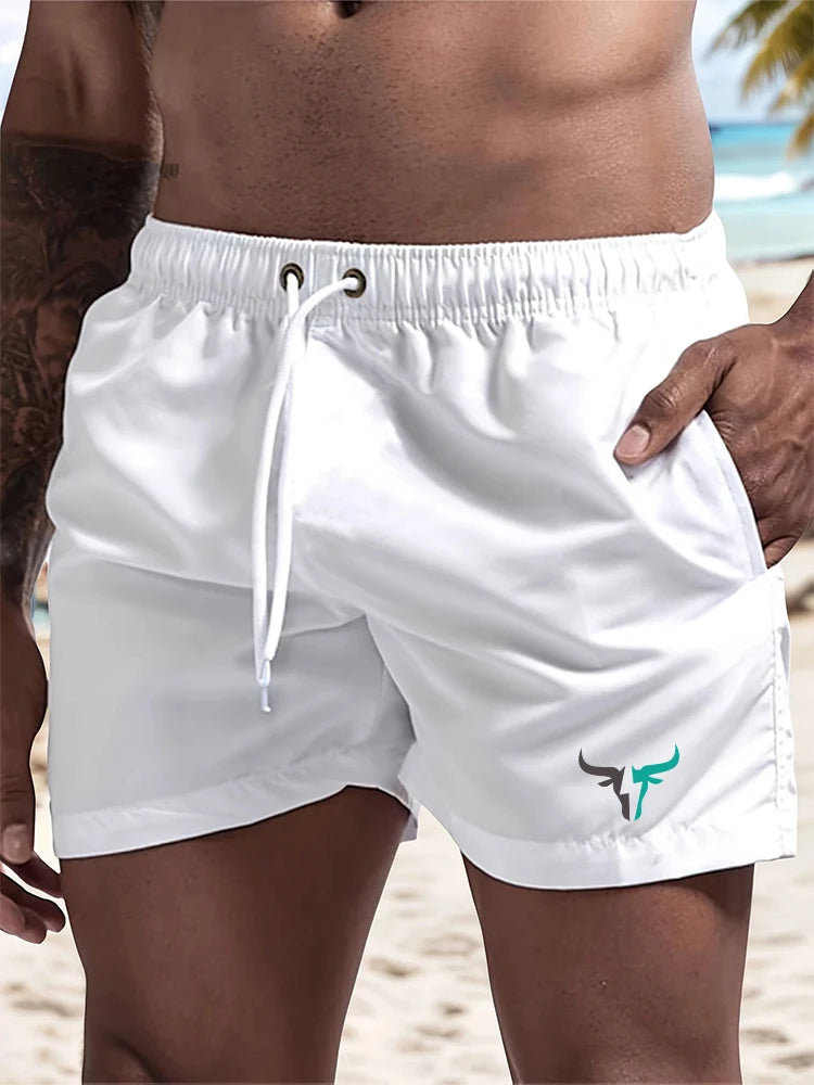 White quick-drying men's swim shorts worn by a person standing on a beach.