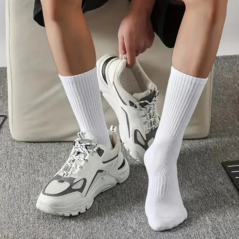 Une personne porte des chaussettes en tube tricotées blanches et des baskets blanches, assise sur un canapé gris.
