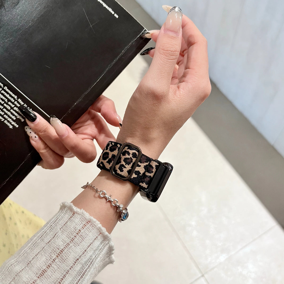 A hand is holding a black leopard print silicone watch band on a wrist, next to a box.