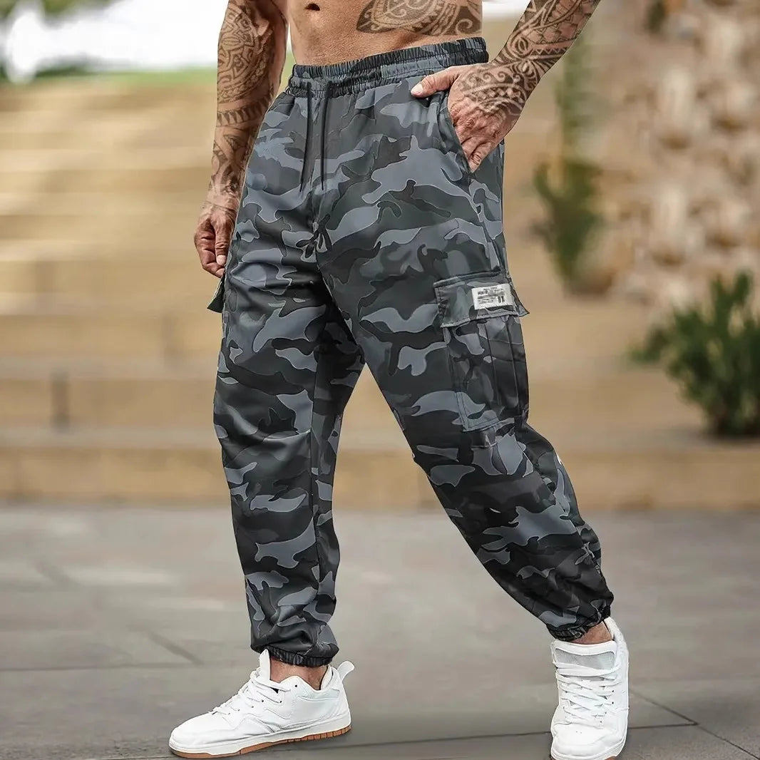 Un homme portant un pantalon cargo de camouflage, debout à l'extérieur.