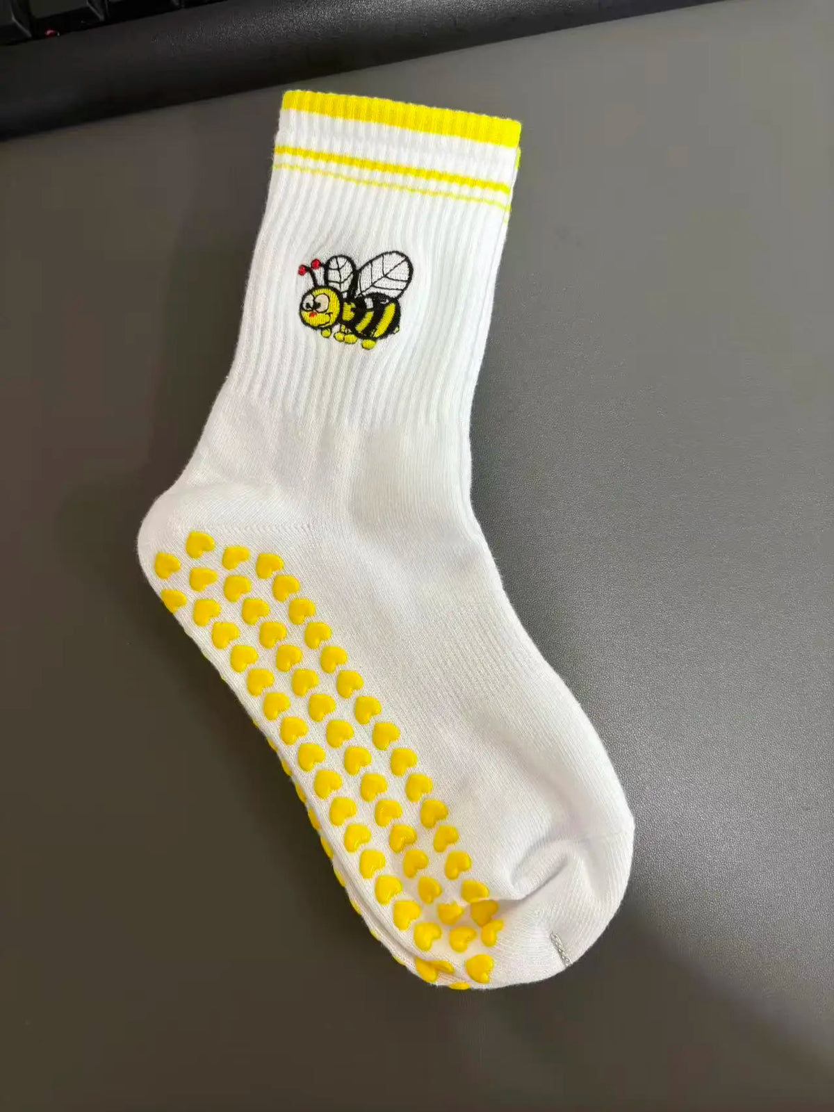 Weiße Strick-Yoga-Socken mit gelbem Zierrand und schwarzem Bienenmotiv.
