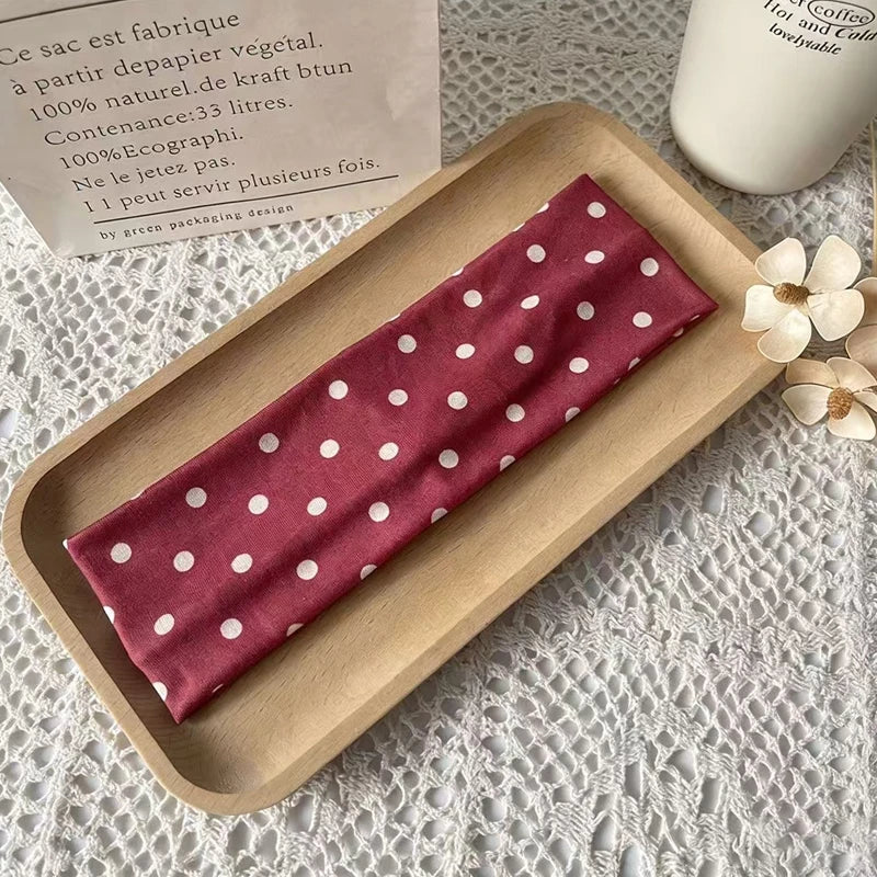 Ein dunkelrotes Polka-Dot-Stoff-Haarband wird auf einem Holztablett neben einem Etikett präsentiert.