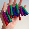 A hand holds a collection of colorful aluminum survival whistles attached to metal clasps.