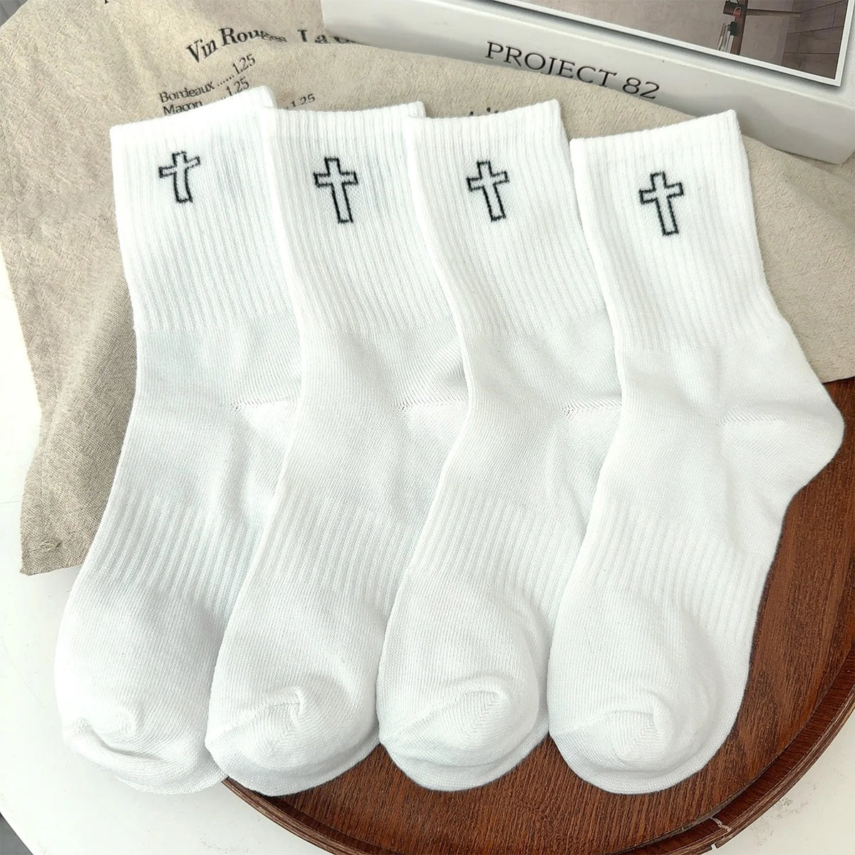 A set of white men's high-cut breathable casual crew socks with a cross design displayed on a wooden surface.