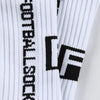 Close-up of white and black athletic soccer socks with a vertical striped pattern and a black logo detail.