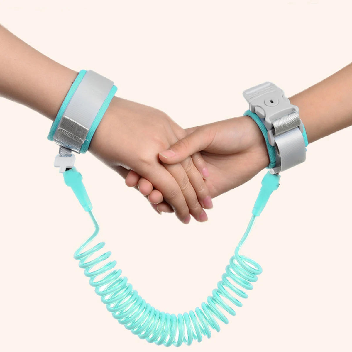 A hand is holding a turquoise adjustable child safety harness and leash, featuring silver buckles.