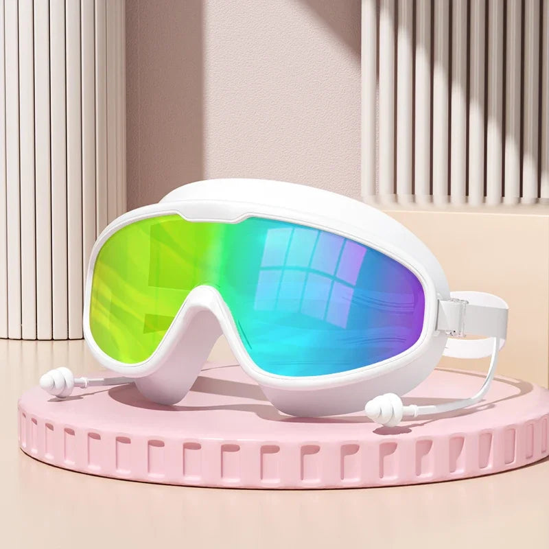 Gafas de natación blancas antiempañante con lentes verdes brillantes y azules sobre una superficie rosa.