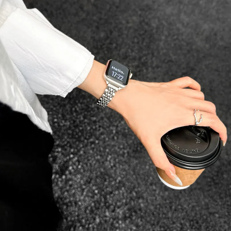 A hand wearing a silver stainless steel watch band on a smartwatch with a black face and a white cuff.