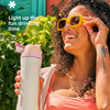 Eine Frau hält eine Owala isolierte Wasserflasche im Freien und lächelt, trägt eine Sonnenbrille.