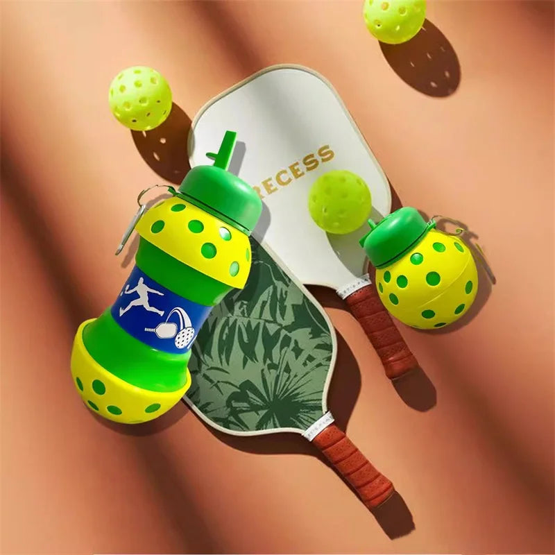 A green and yellow leakproof silicone sports water bottle is shown next to a tennis racket and tennis balls.