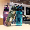 Three leak-proof sports water bottles in purple, green, and blue glass with black lids displayed on a wooden surface.