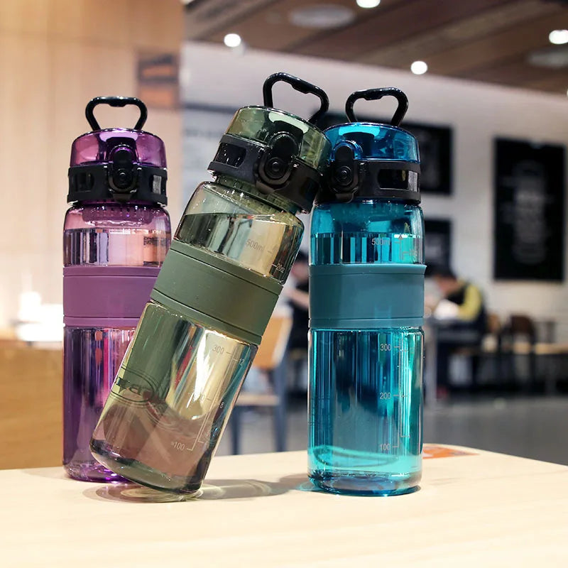 Three leak-proof sports water bottles in purple, green, and blue glass with black lids displayed on a wooden surface.