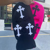 A black knit beanie hat with white cross embroidery is displayed next to a bright pink knit beanie hat.