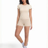 A woman models a beige performance workout set consisting of a short-sleeved top and matching shorts.