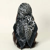 A black and gray leopard print satin square scarf tied around dark hair.