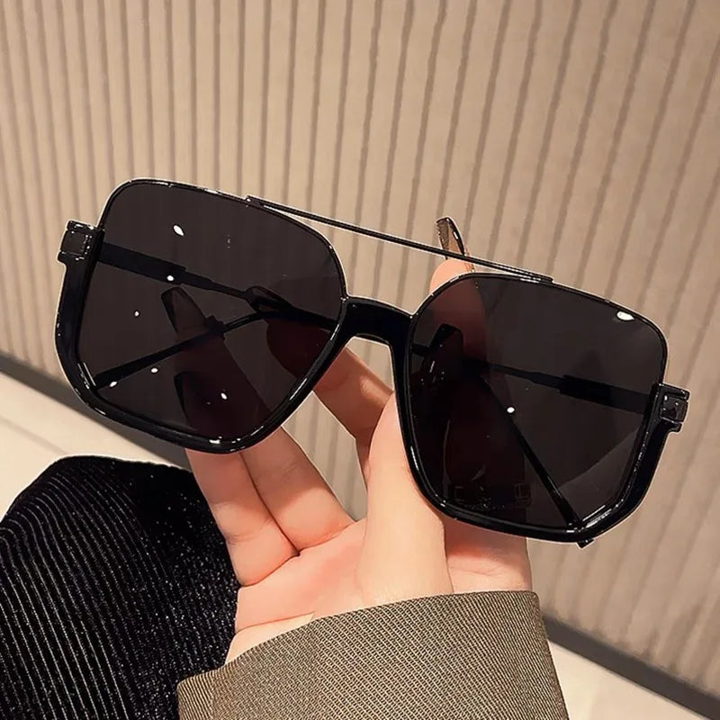 A hand holds a pair of black UV400 double beam sunglasses against a light background.