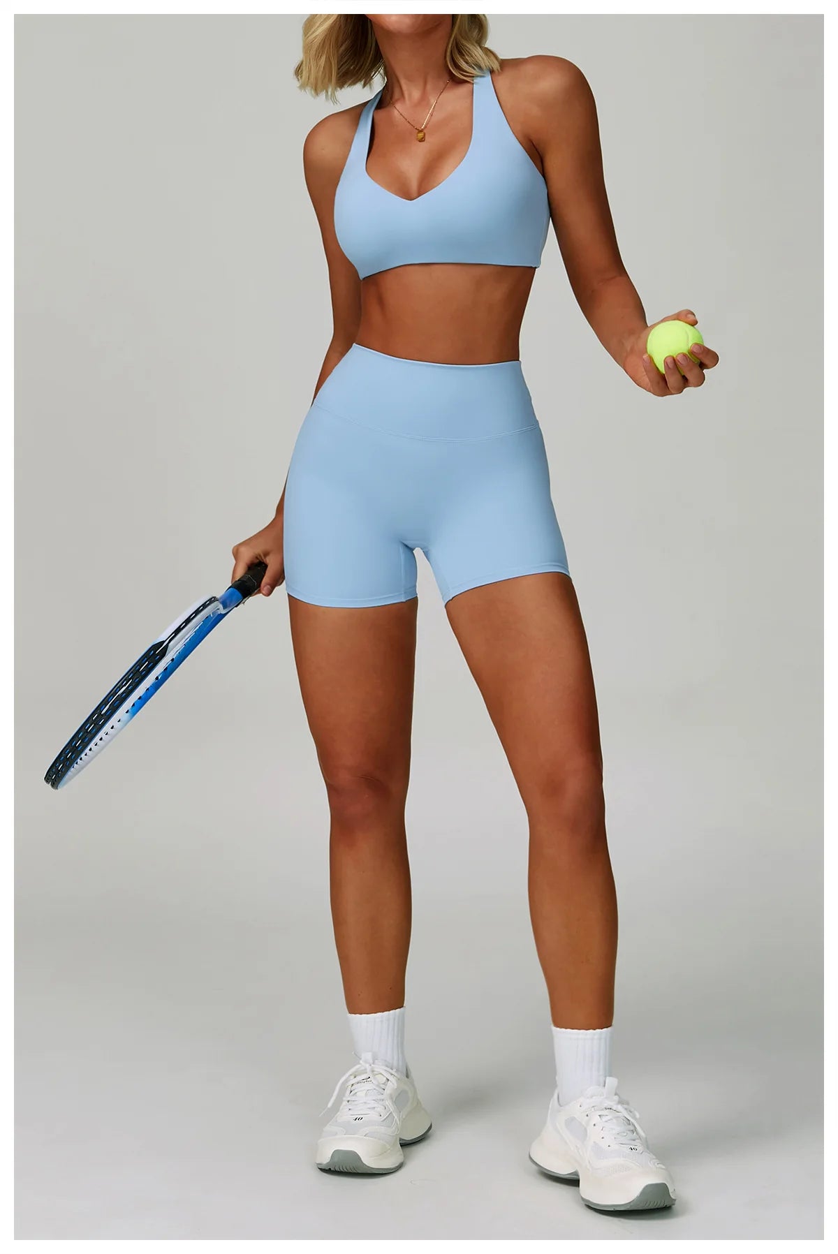 A woman models a light blue padded sport yoga bra and matching brief on a studio background.