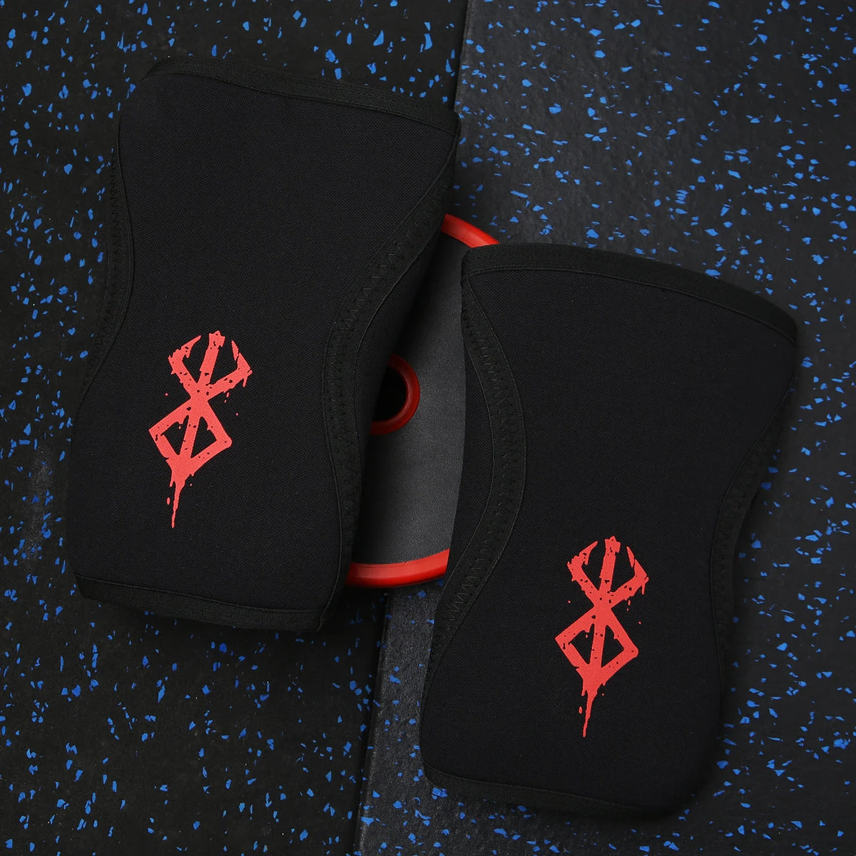 Une paire de genouillères noires avec des motifs de dragon rouge, posées sur une surface bleu foncé texturée.