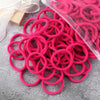 A pile of pink elastic hair bands in a clear plastic bag and loose, resting on a gray surface.