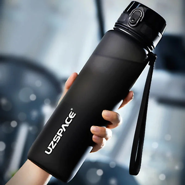 Une main tient une bouteille d'eau sportive noire et réutilisable en Tritan avec une corde, sur un arrière-plan flou.