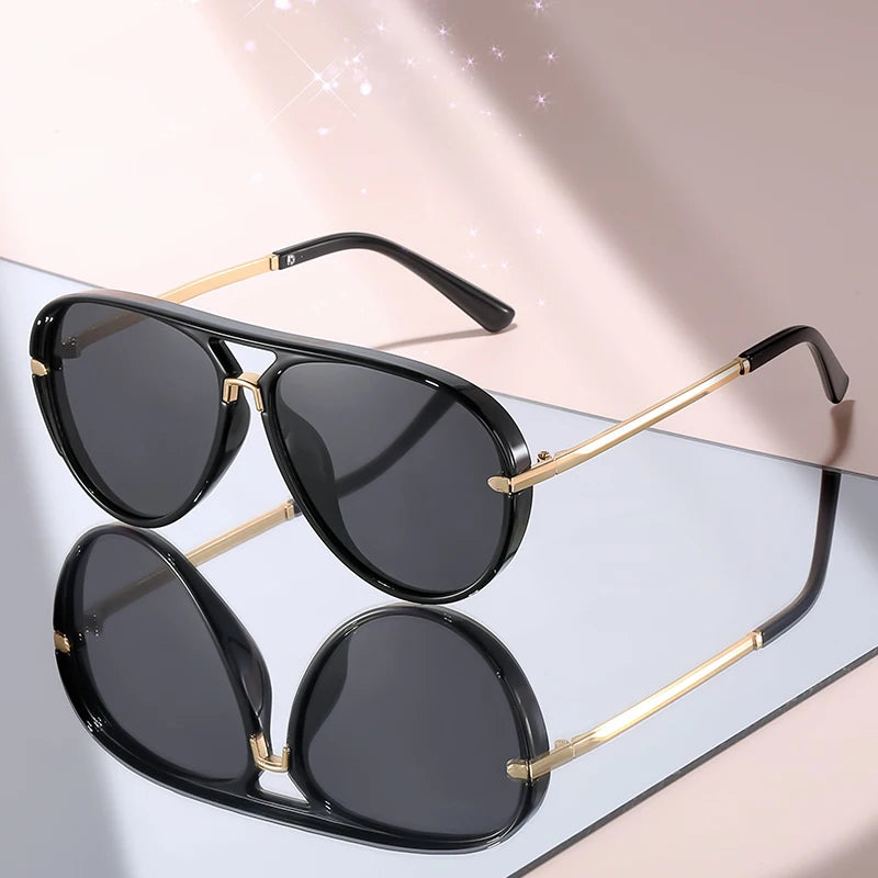 Black gradient aviator sunglasses with gold accents displayed on a light surface.