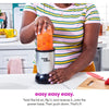 Una mujer usando una licuadora Magic Bullet plateada en una encimera blanca.