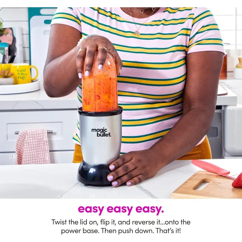 Una mujer usando una licuadora Magic Bullet plateada en una encimera blanca.